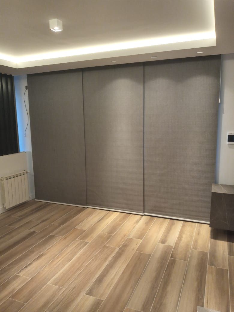 Habitación vacía con suelo de madera, paneles de pared grises y una luz empotrada en el techo.