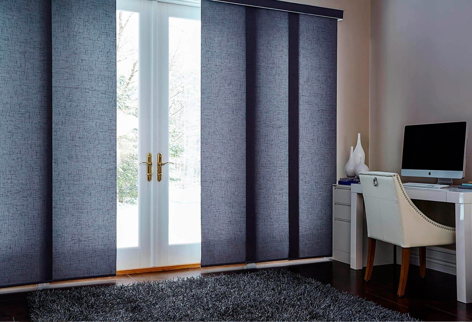 Sala de estar con cortinas azules, puertas de cristal, escritorio, silla y ordenador a la derecha.