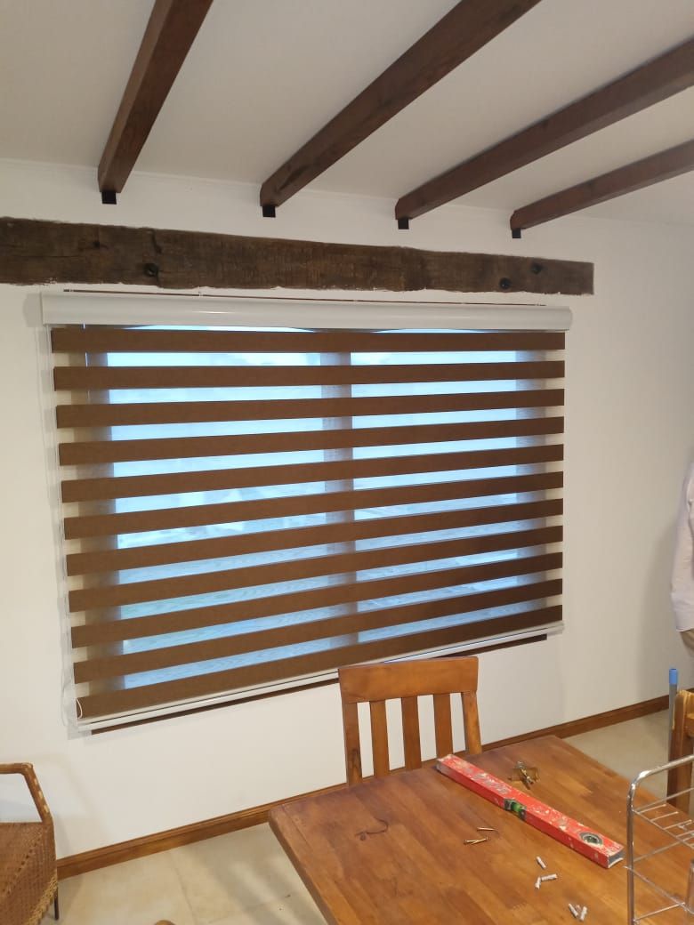 Vigas de madera en el techo, sobre una ventana con persianas de rayas marrones