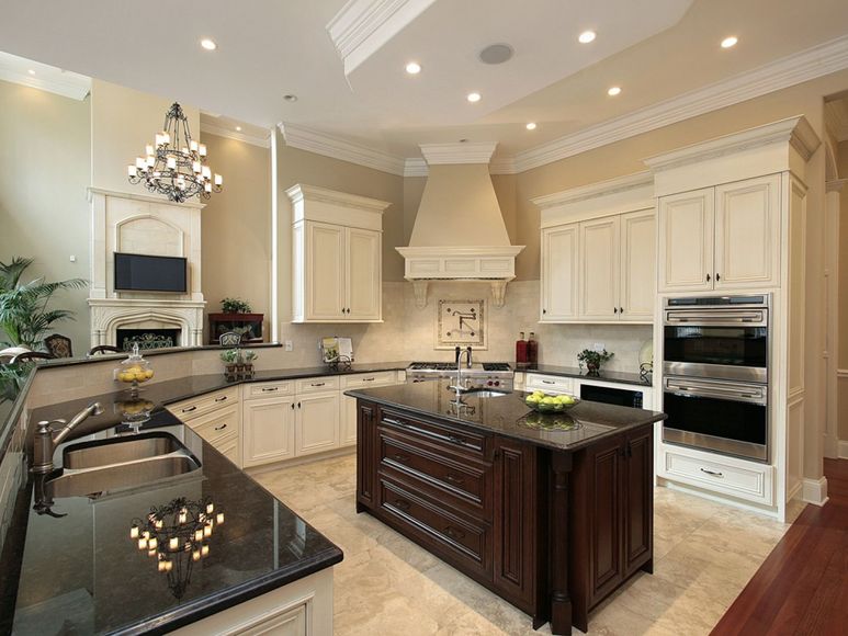 Elegant cream-colored kitchen with a dark island, built-in ovens, and chandelier lighting