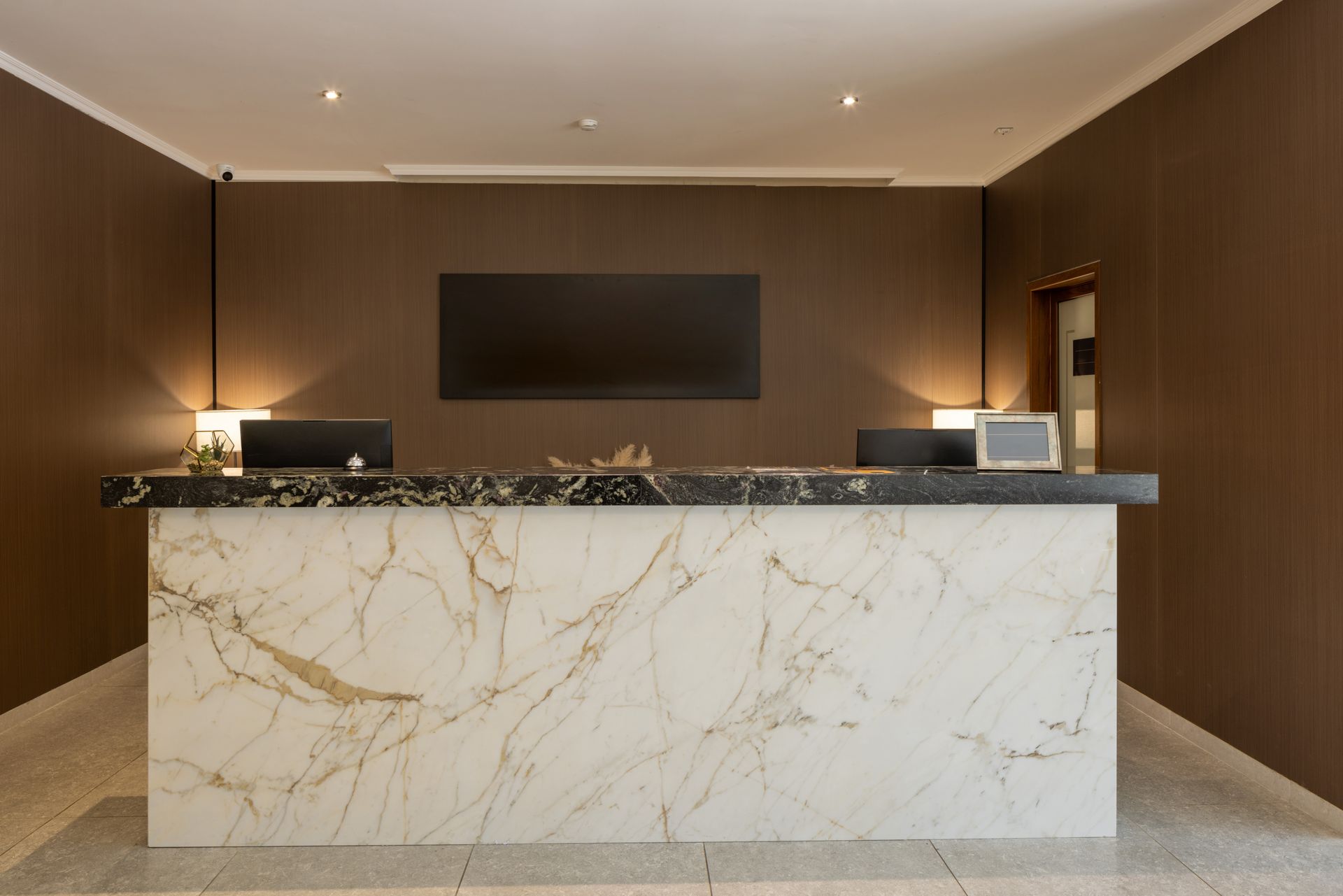 Modern hotel lobby reception desk with white marble front, dark wood walls, and warm lighting
