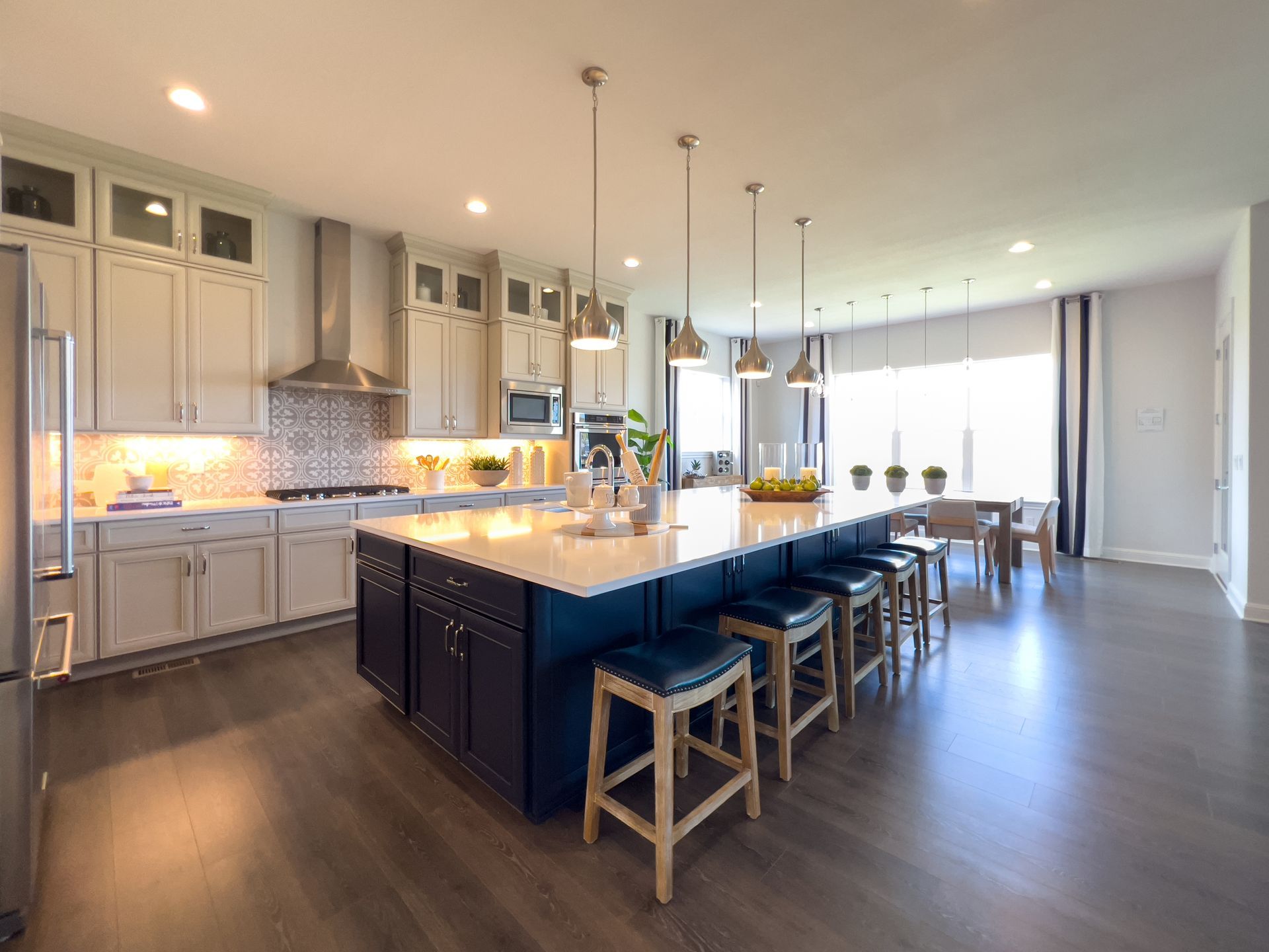 Spacious modern kitchen with a large island, pendant lights, and barstools beside bright windows.