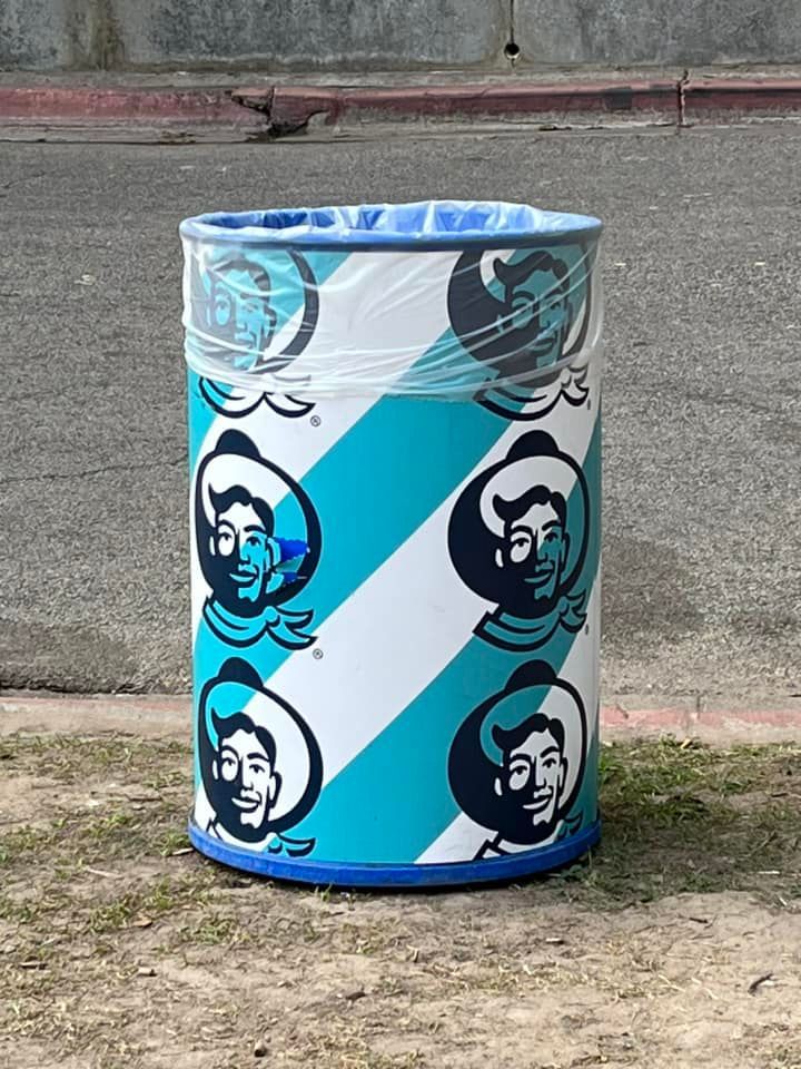 Blue and white cylindrical bin with repeated black face logos on a pavement background