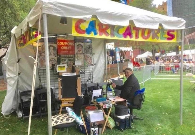 Colorful caricature booth at a fair, with an artist seated under a tent and supplies on the table