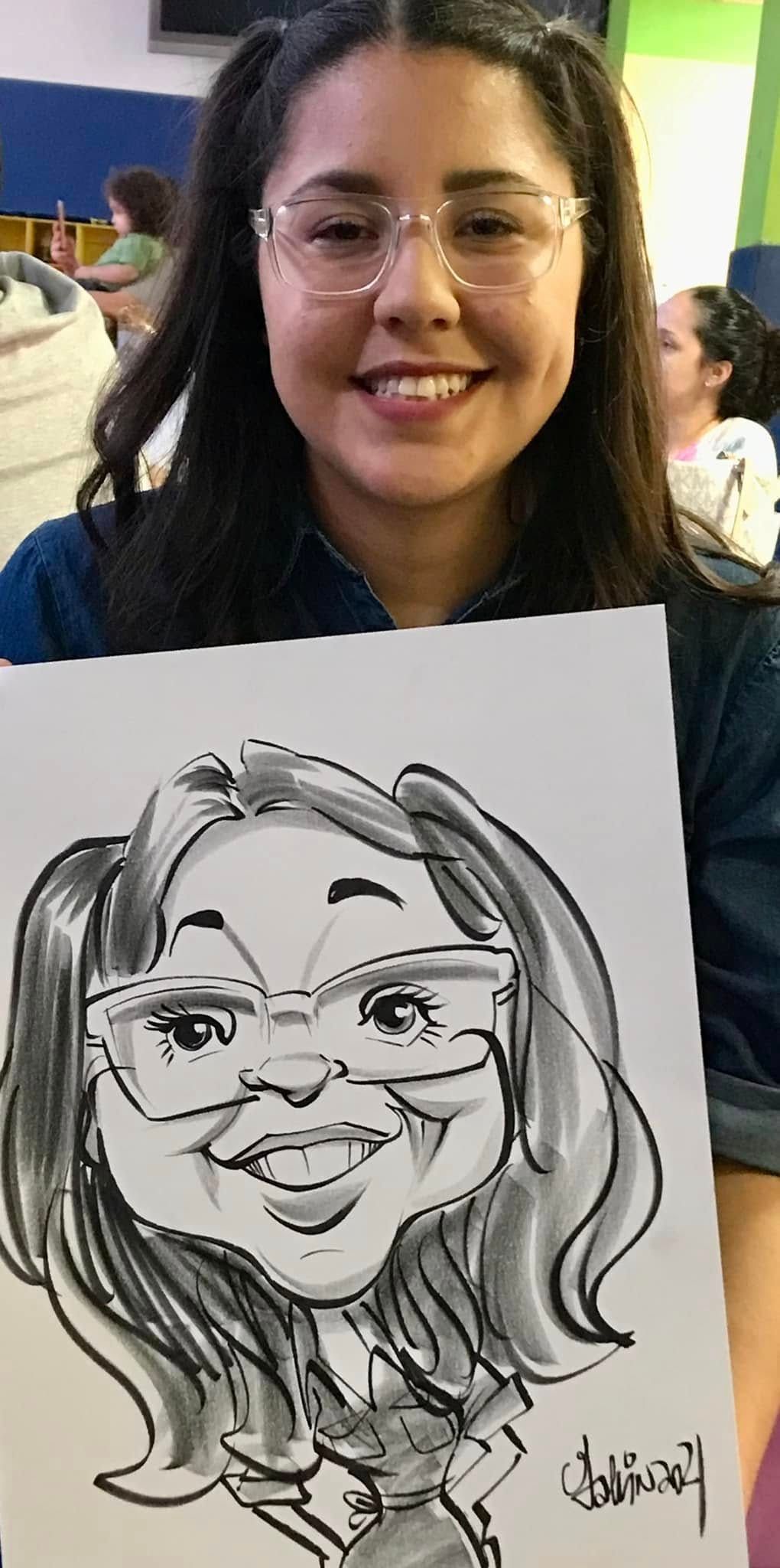 Woman holding a black-and-white caricature portrait of herself, smiling at the camera.