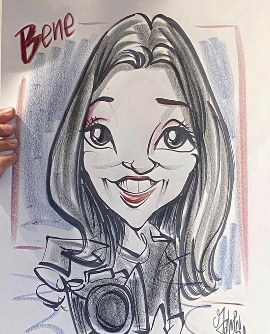 Caricature portrait of a smiling person with long dark hair, holding a camera, signed “Bene.”