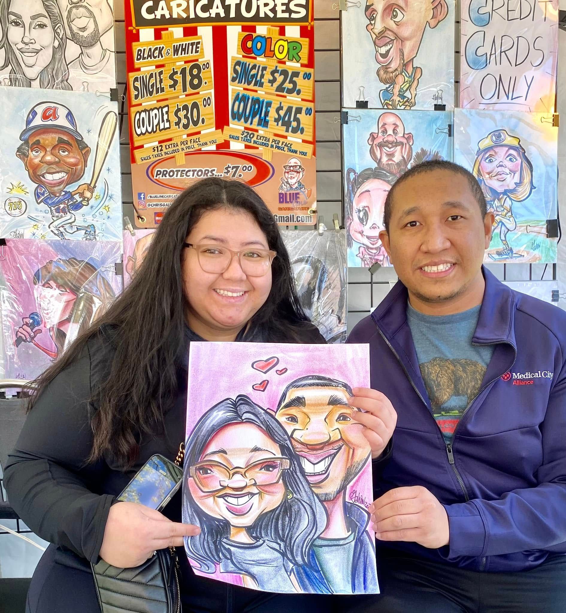 Two people holding a colorful caricature portrait in front of a wall of other caricatures.