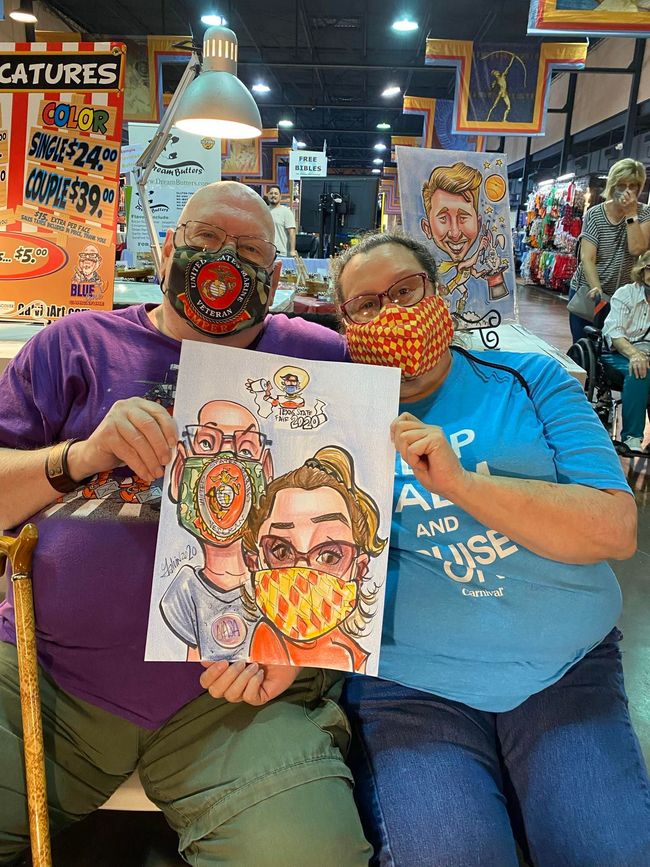 Two people in masks holding a caricature drawing at a crowded indoor event.