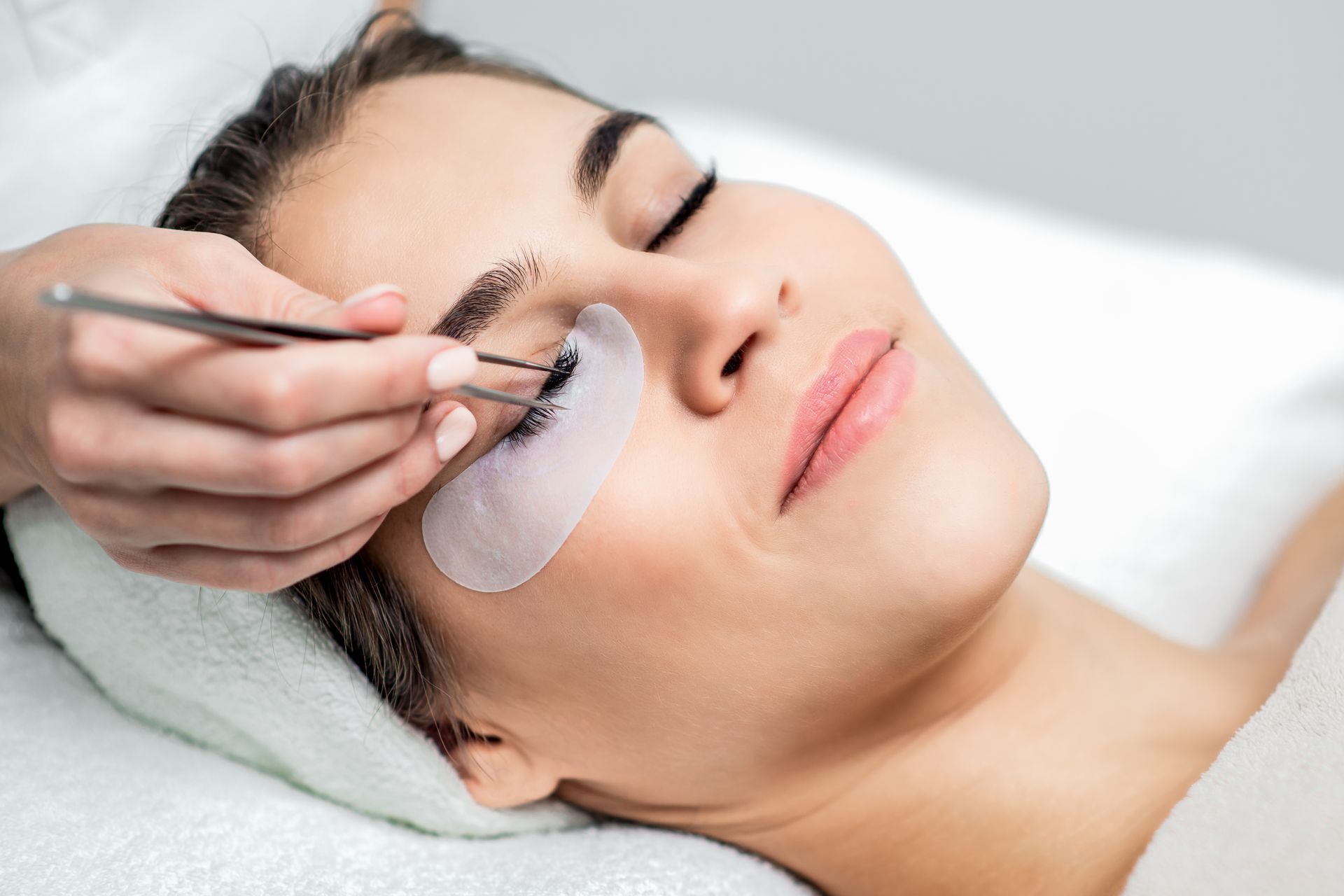 Beauty technician applying eyelash extensions to a client lying on a treatment bed