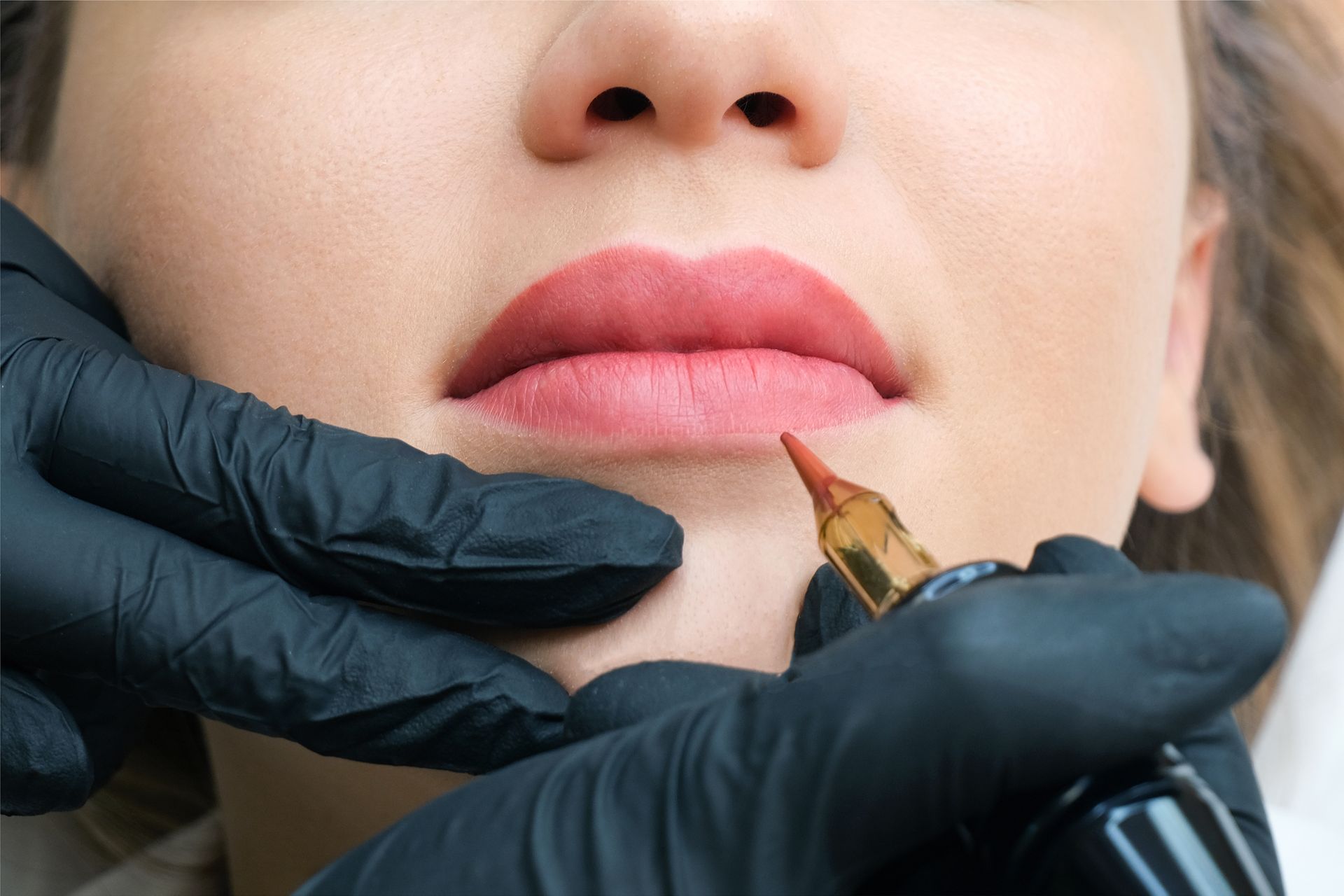 Gloved hands applying makeup to a woman's lips with a brush, close-up.
