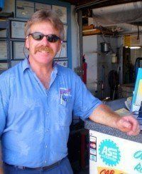 A man with a mustache and sunglasses is standing in front of a counter in a garage.
