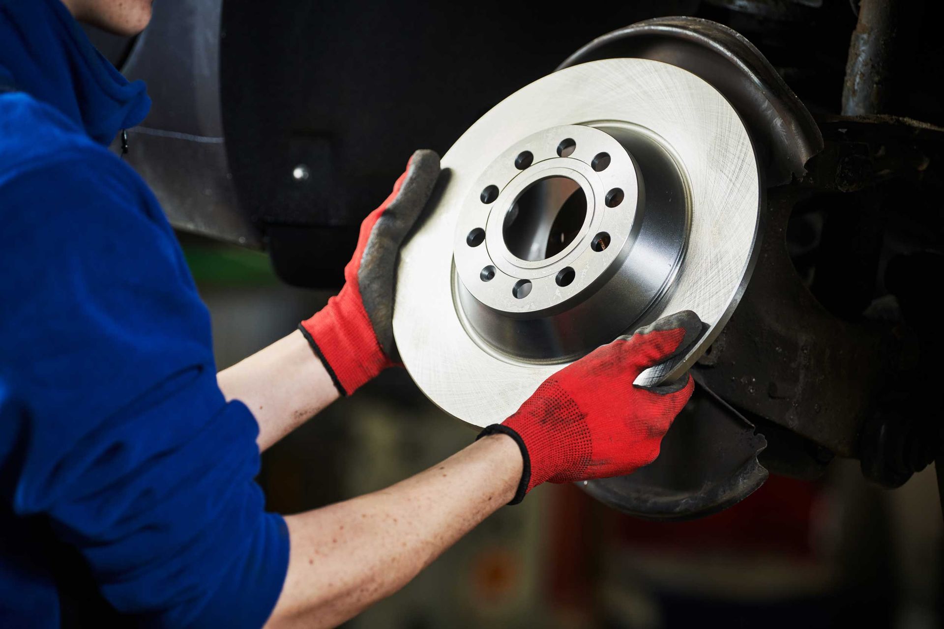 Mechanic installing a brake disc on a car wheel hub while wearing red gloves.