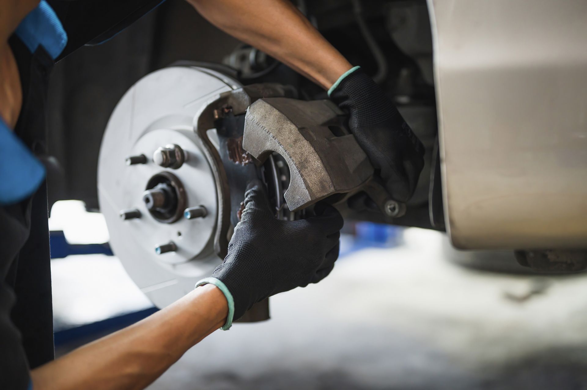An auto mechanic installing a car's front brake caliper and brake pads. An auto mechanic installing a car's front brake caliper and brake pads.