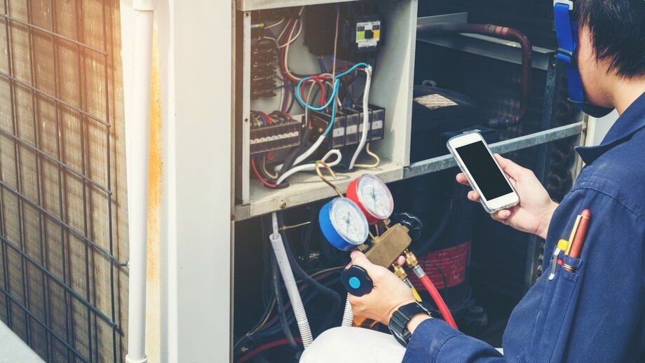 HVAC technician repairing outdoor unit, using gauges and a smartphone.