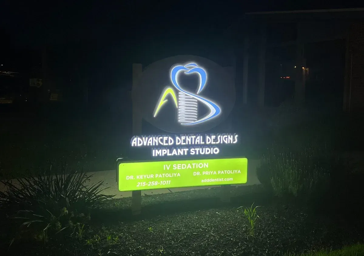 Neon sign for an advanced dental and implant studio glowing blue and green at night.