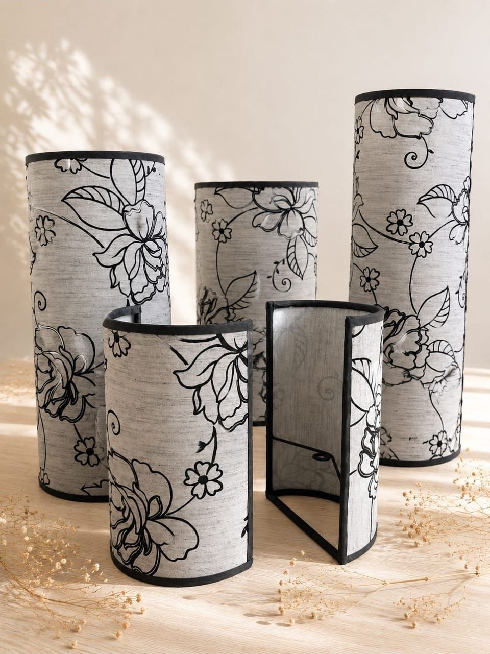 Cinco portavelas cilíndricos con estampado floral en blanco y negro sobre una superficie clara.