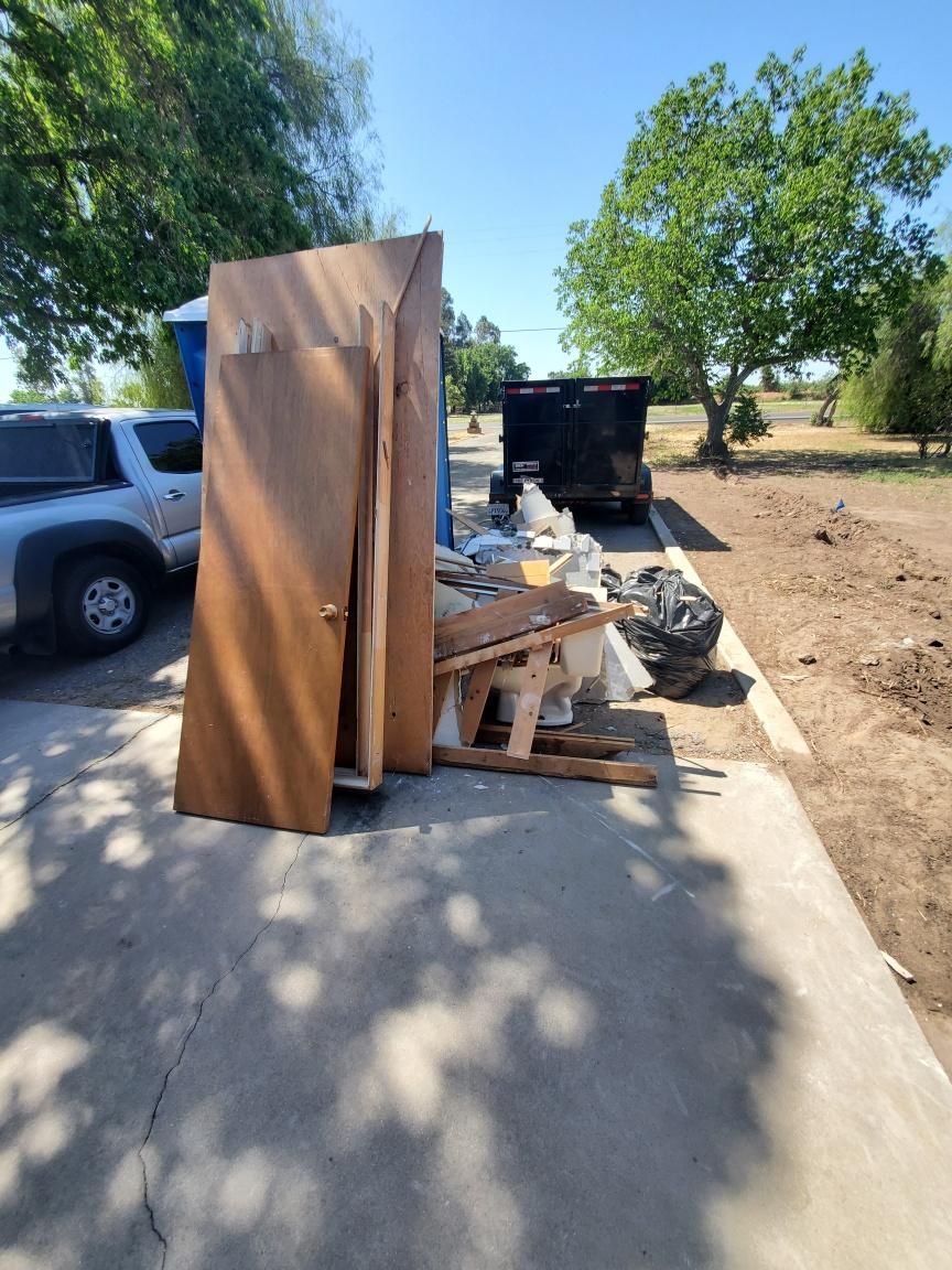 A white pickup truck parked next to a pile of construction debris, including wood doors, frames, and trash on a driveway.