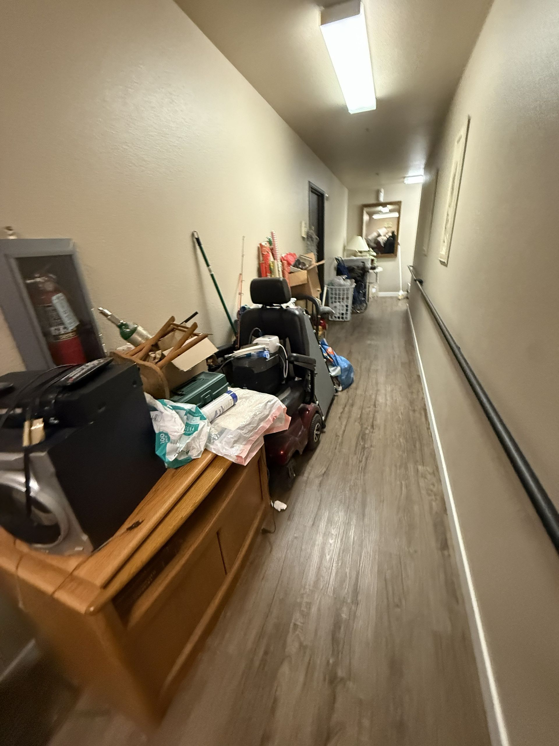 A narrow hallway with a wooden console table, clutter, and a mobility scooter blocking the pathway.
