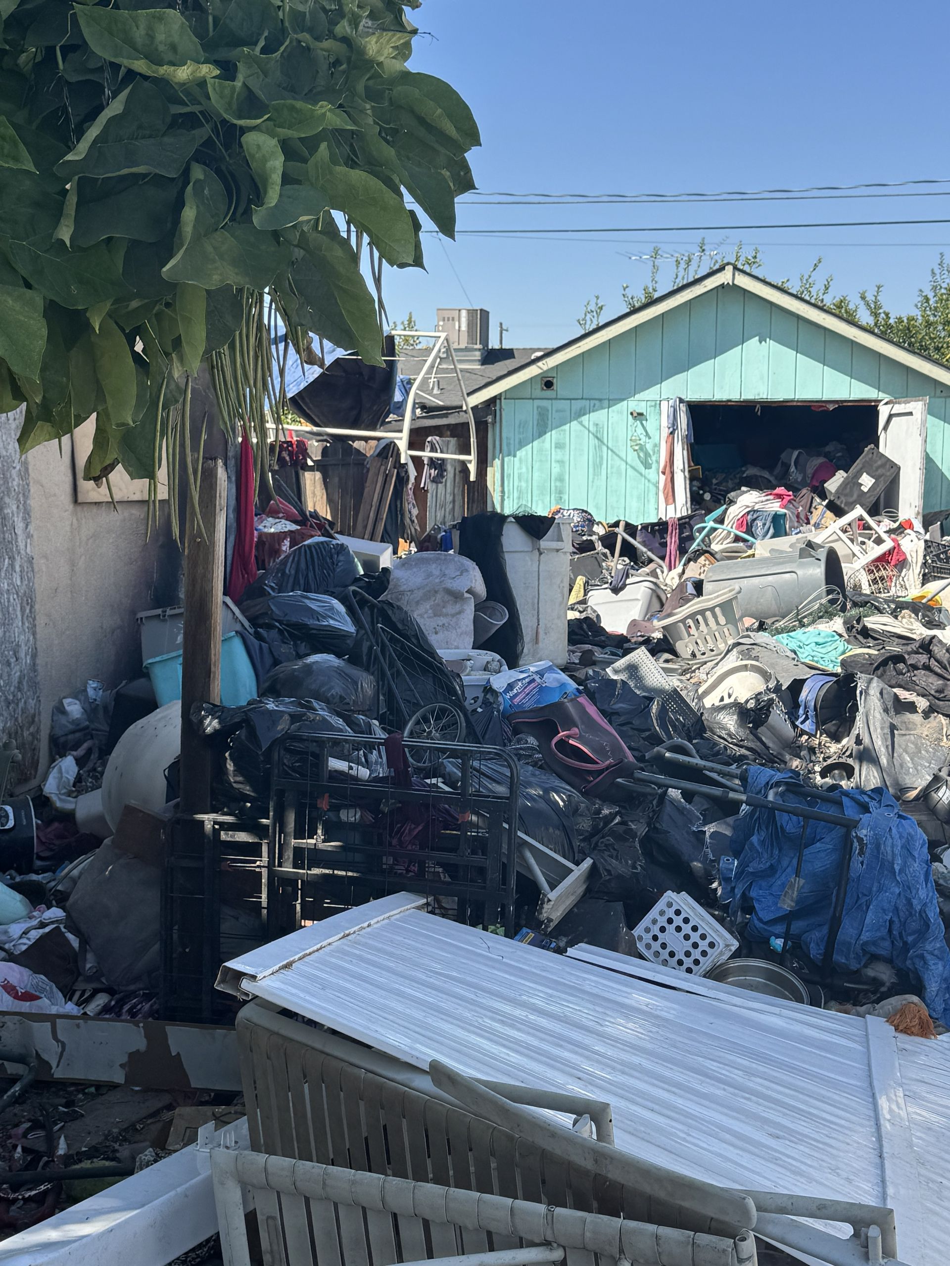A large pile of trash and discarded household items fills the yard in front of a turquoise detached garage.