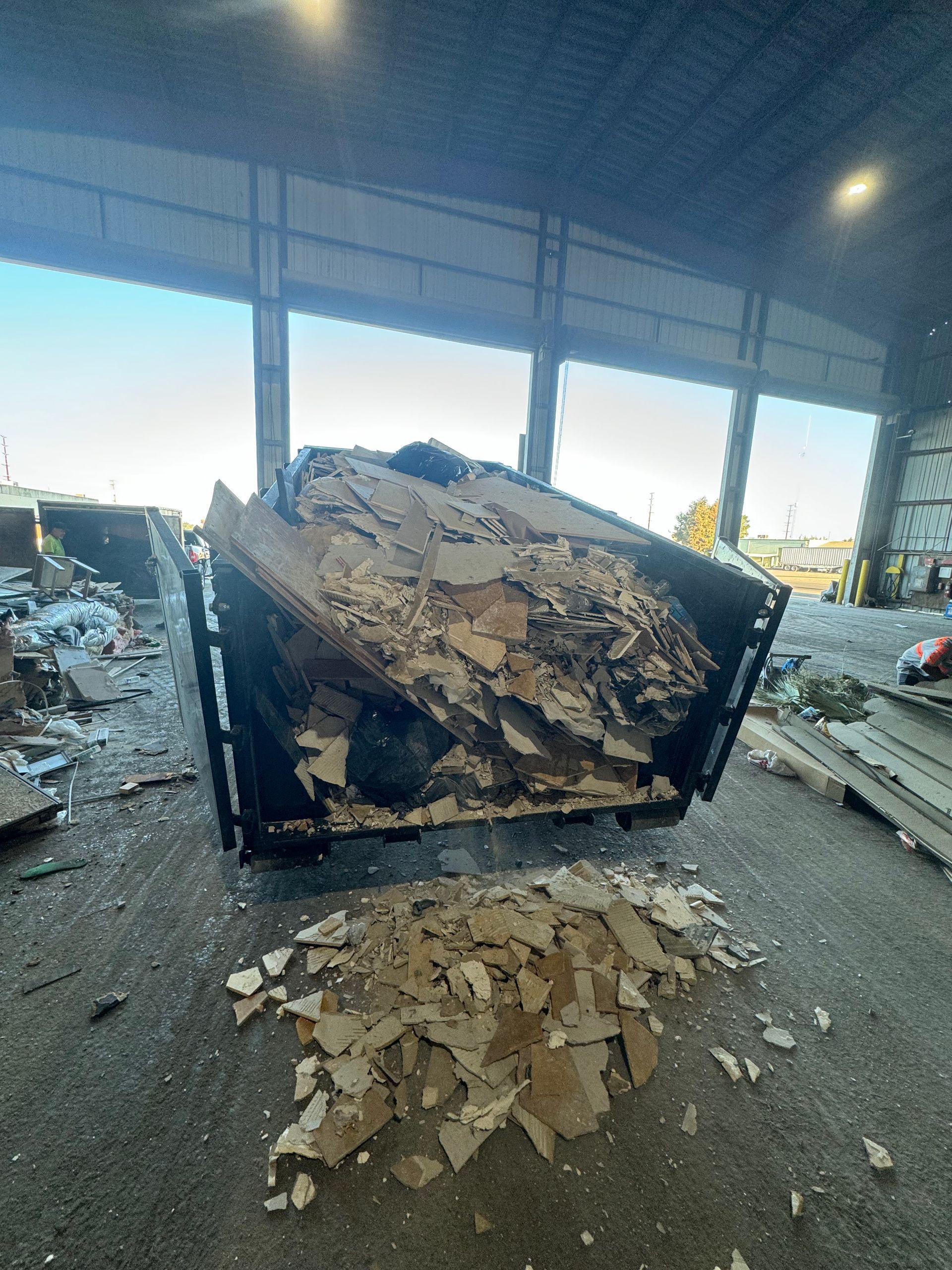 A dumpster piled high with construction debris, specifically pieces of drywall, in a large warehouse facility.