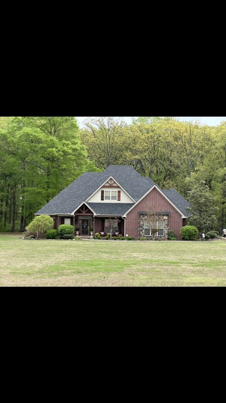A large brick house with a black roof is sitting on top of a lush green field.