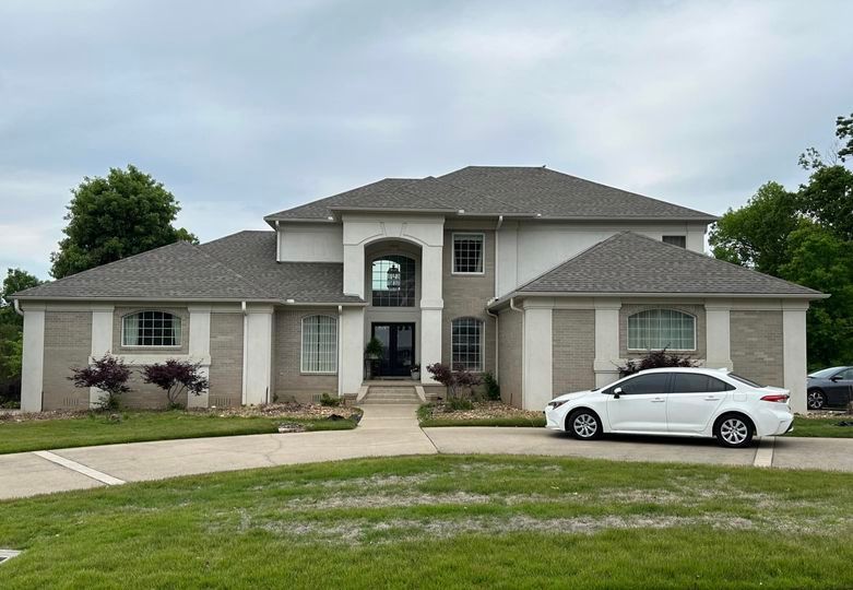 A white car is parked in front of a large house.