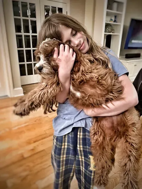 Child hugging a fluffy brown dog in a bright kitchen, smiling with eyes closed