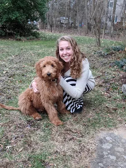 Woman smiling with a curly brown dog sitting together outdoors in a grassy yard