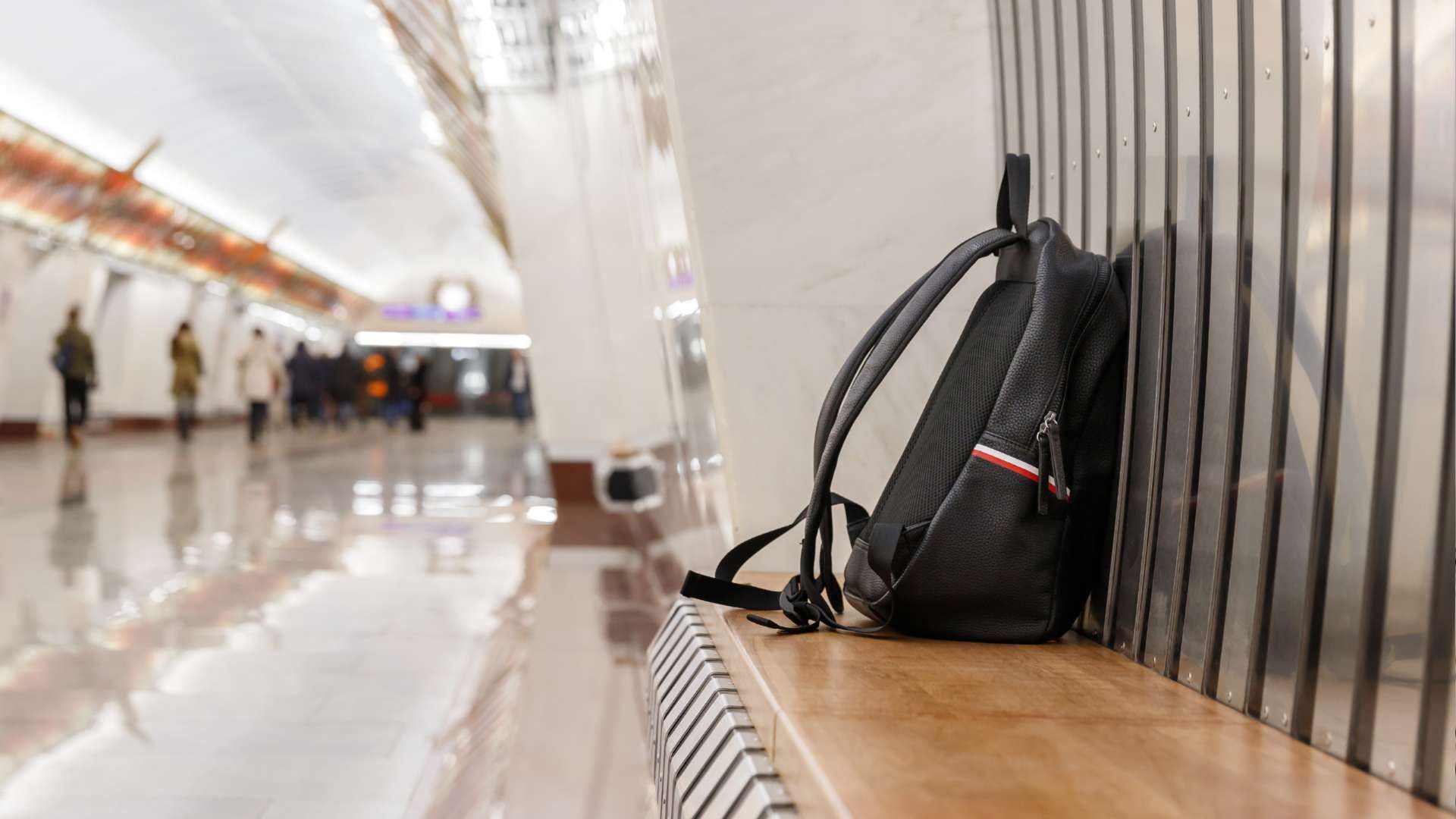 Black backpack on a bench in a bright airport corridor, with people blurred in the background