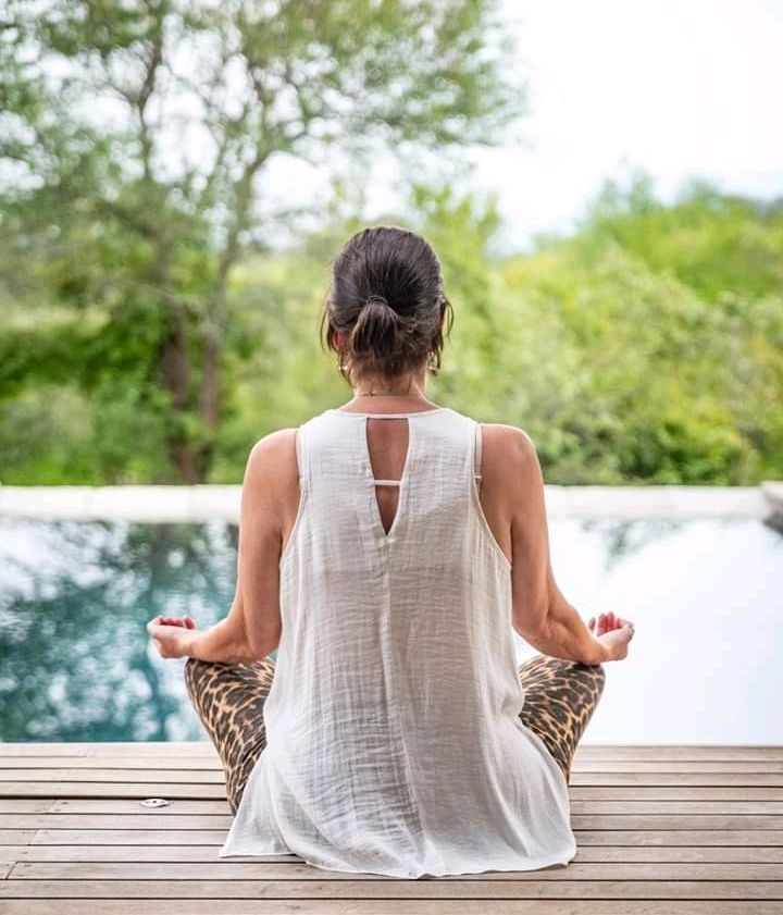 A woman is sitting in a lotus position on a wooden deck.
