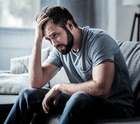 Sad unhappy handsome man sitting on the sofa and holding his forehead while having headache
