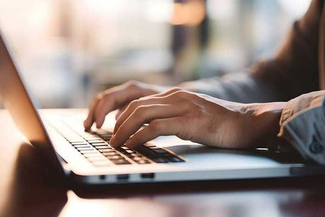 Close up of a business man working on a laptop, typing with his hands for work in office environment home office