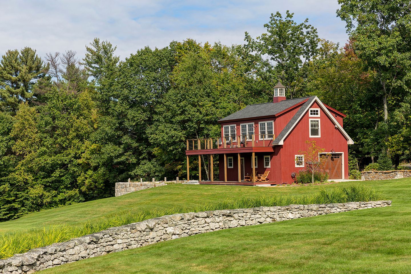 A red house is sitting on top of a lush green hill surrounded by trees.