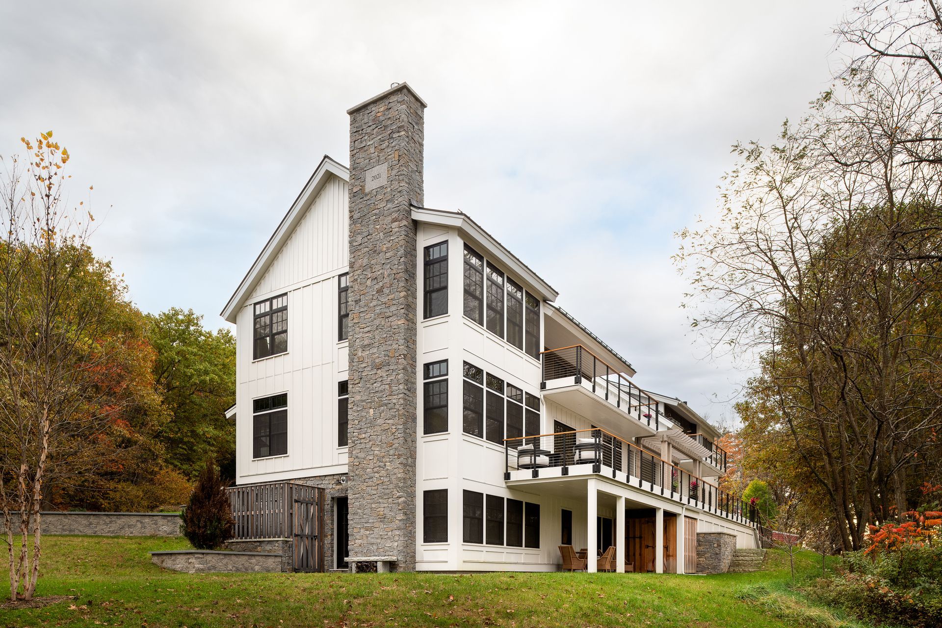 A large white house with a stone chimney is surrounded by trees and grass.