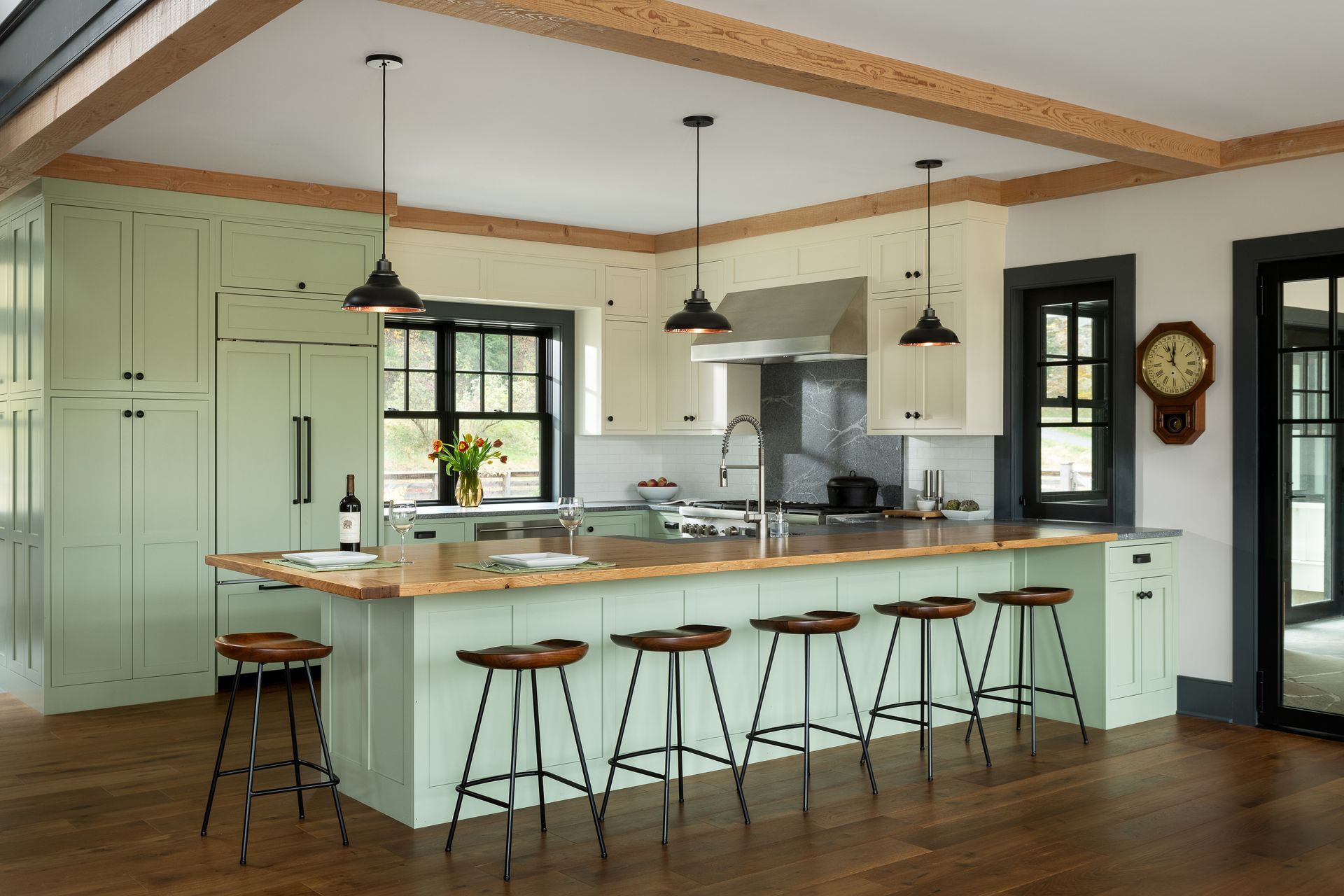 A kitchen with a large island and stools and a clock on the wall.