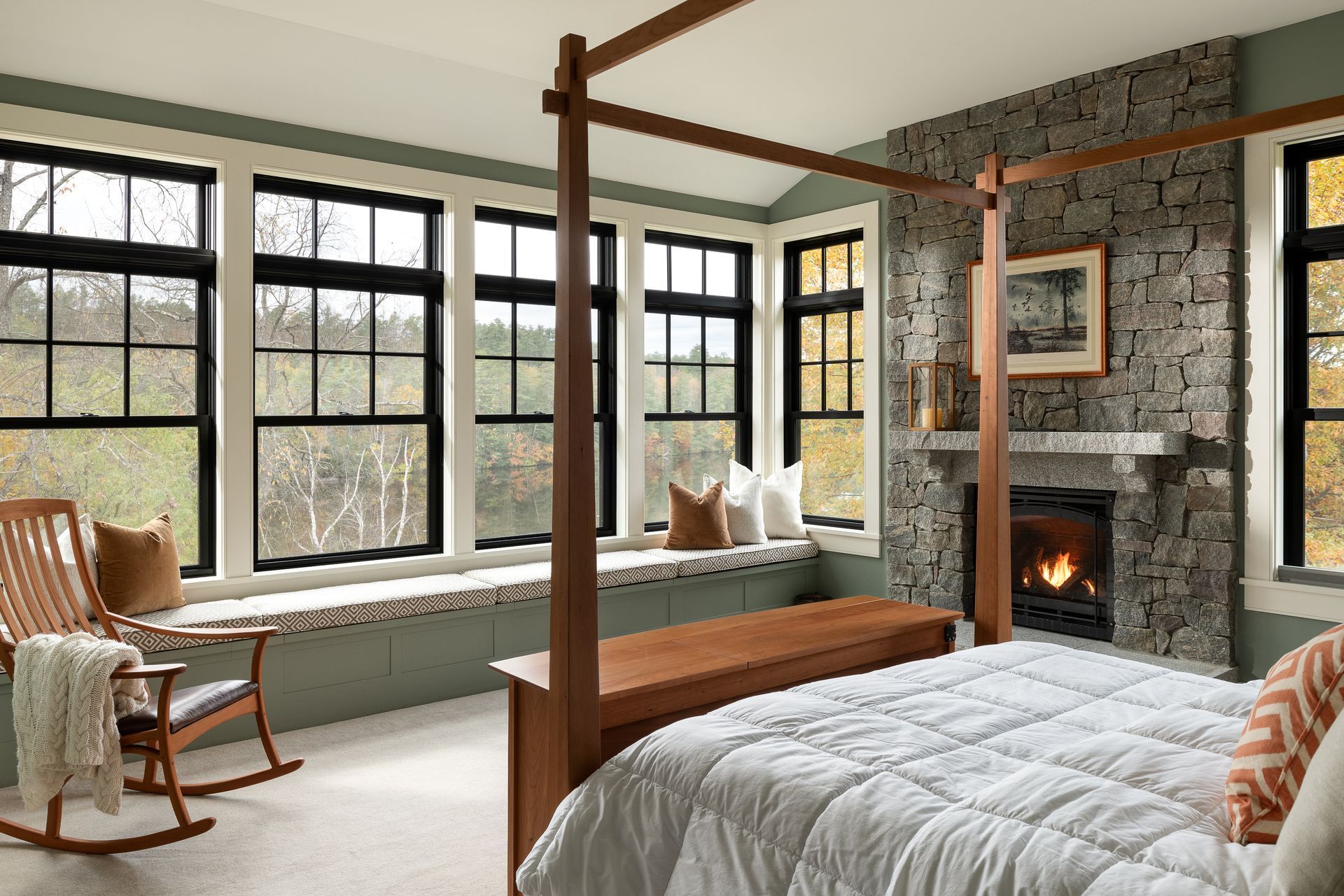 A bedroom with a canopy bed , rocking chair , bench and fireplace.