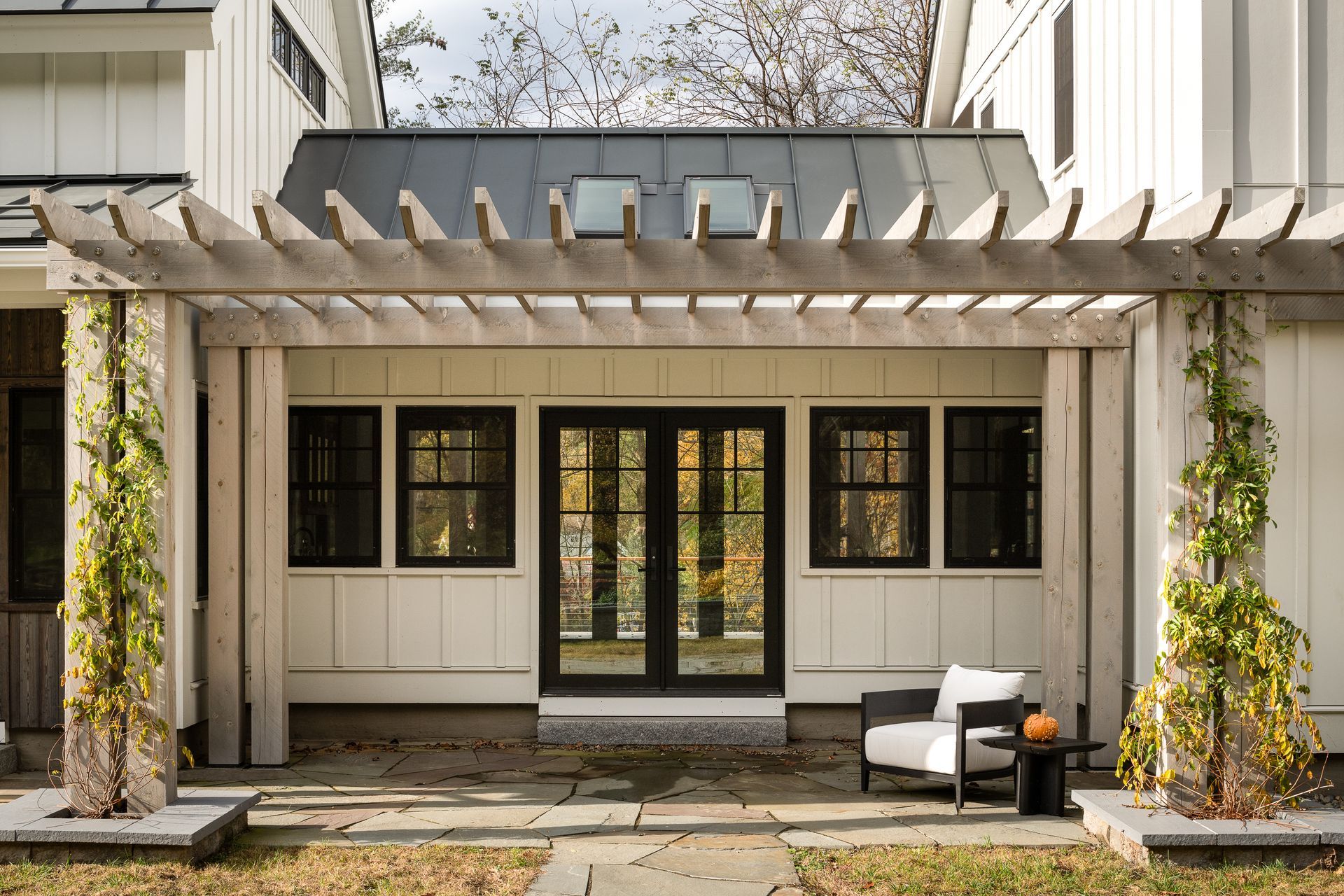 The backyard of a house with a pergola and chairs.