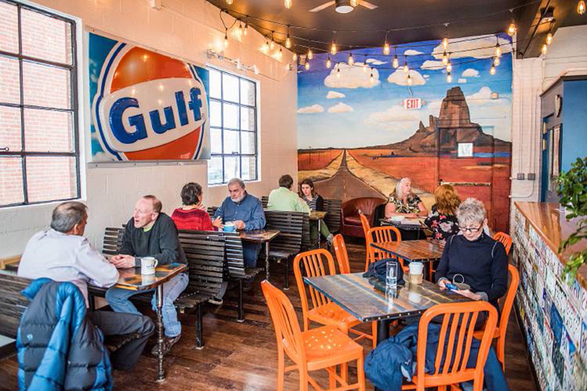 A group of people are sitting at tables in a restaurant with a gulf sign on the wall.