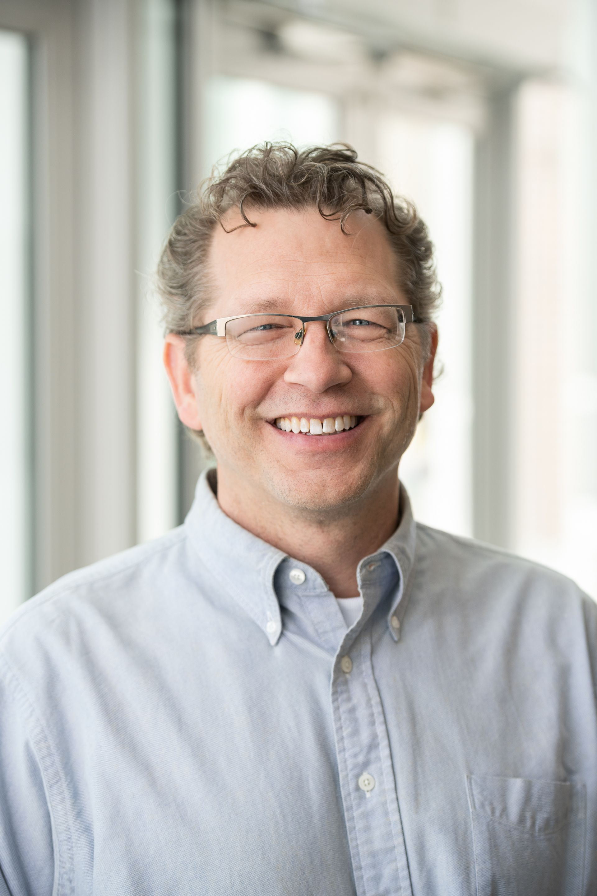 A man wearing glasses and a blue shirt is smiling for the camera.