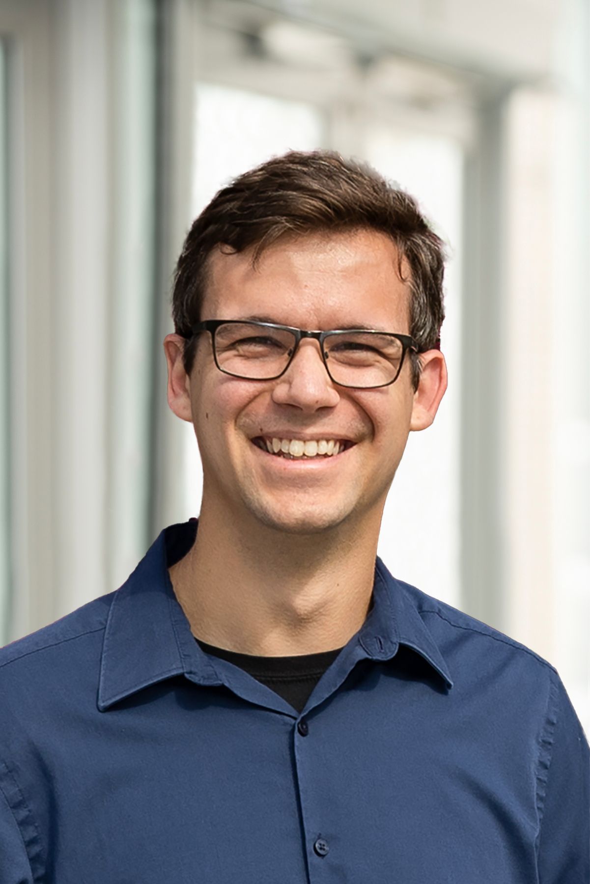 A man wearing glasses and a blue shirt is smiling for the camera.