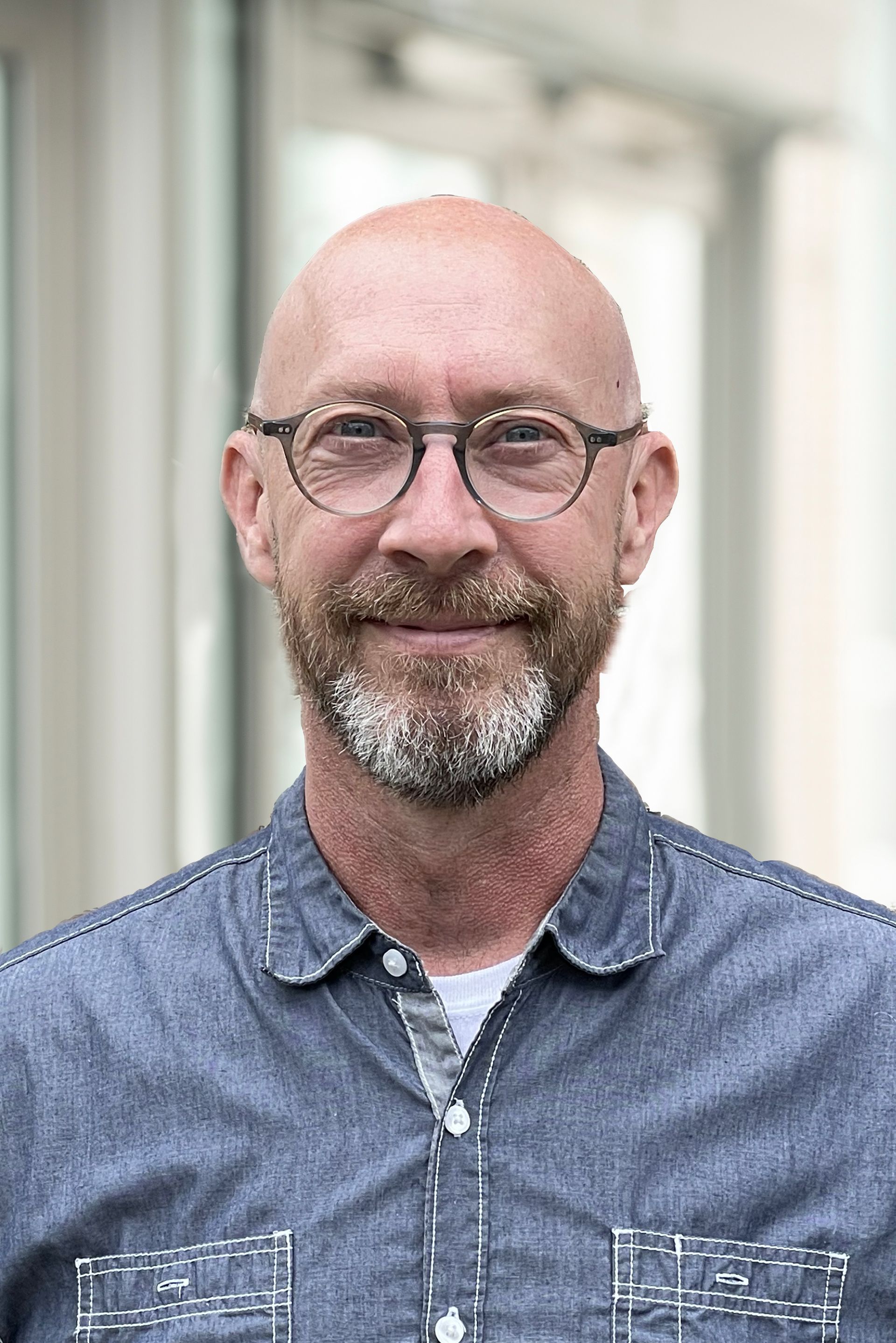 A bald man with a beard and glasses is smiling for the camera.