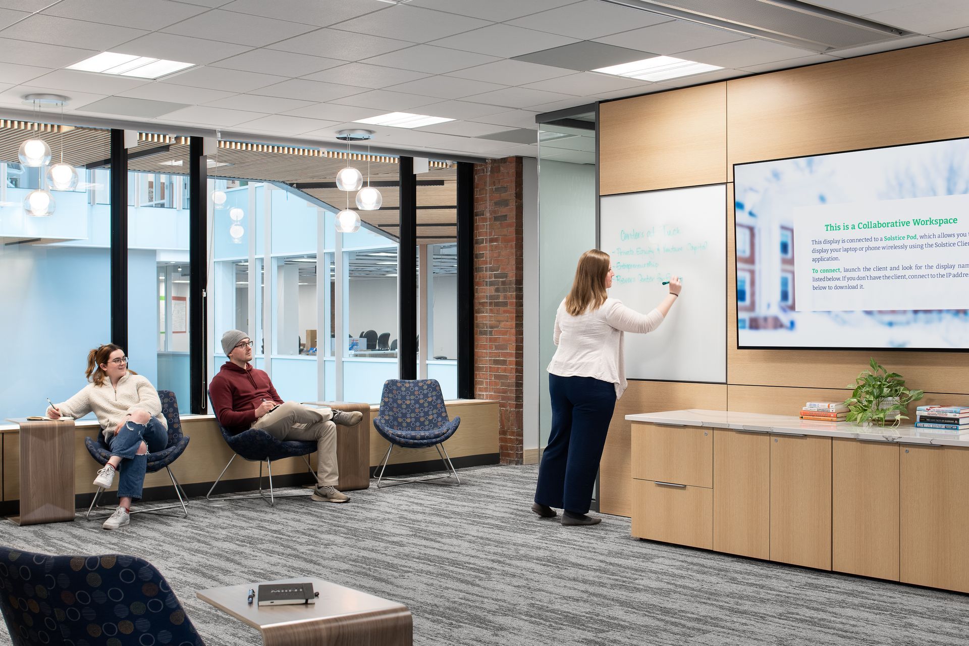 A woman is standing in front of a whiteboard in a conference room.