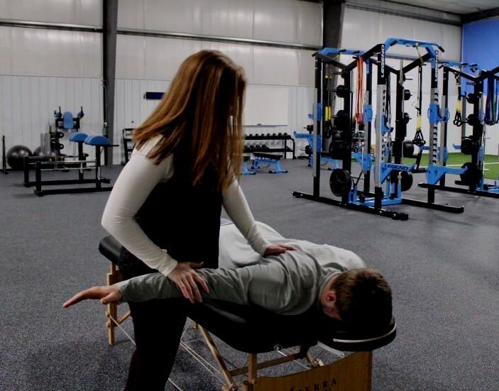 Woman assisting a person lying on a massage table, lifting their arm in a gym.