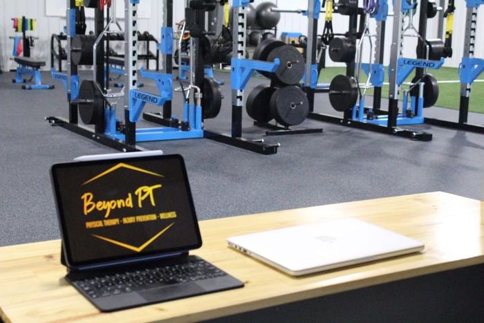 Tablet and laptop on desk in gym with weight racks in background.