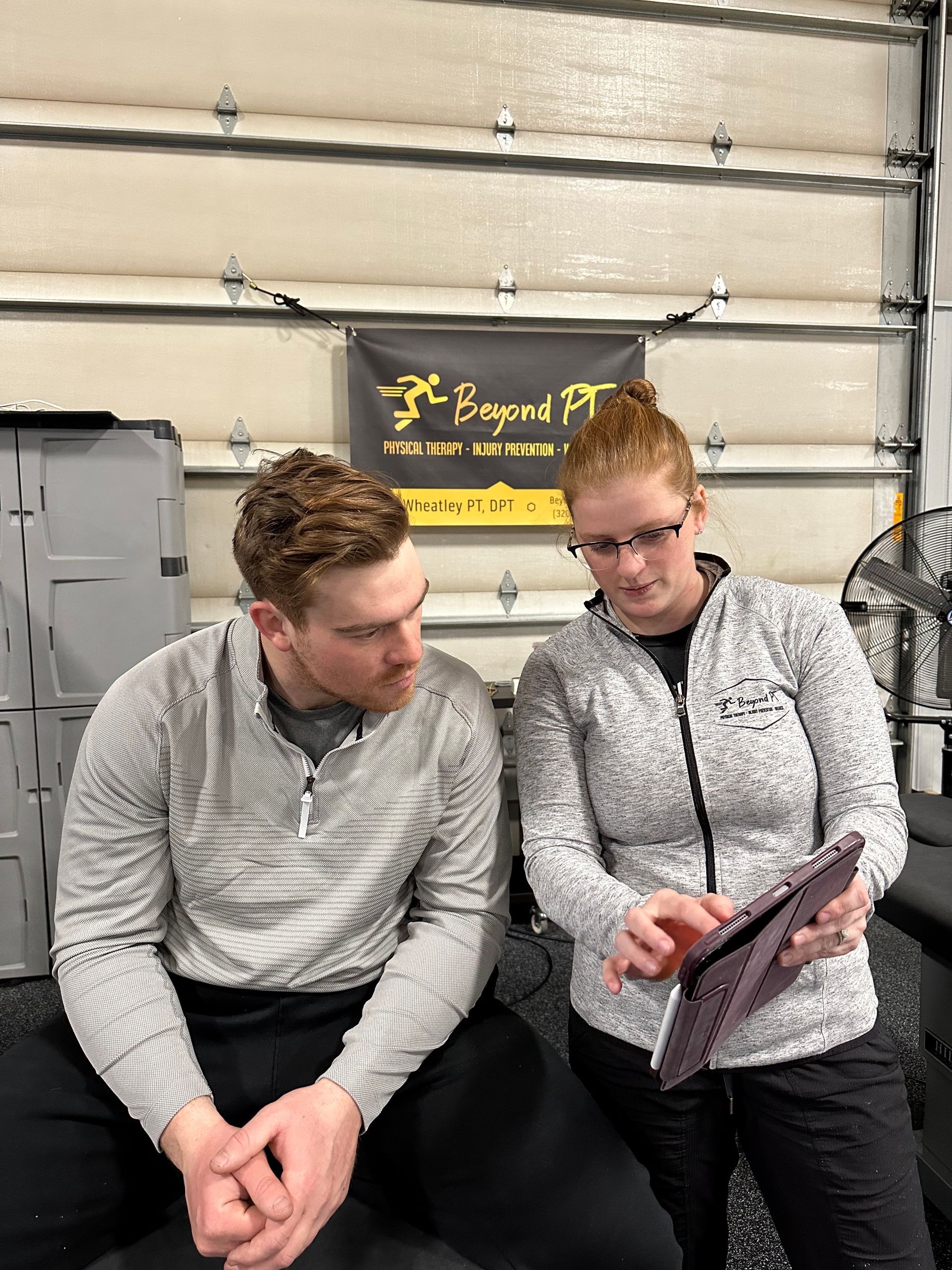 Two people in athletic wear reviewing a tablet in a gym. A logo for 