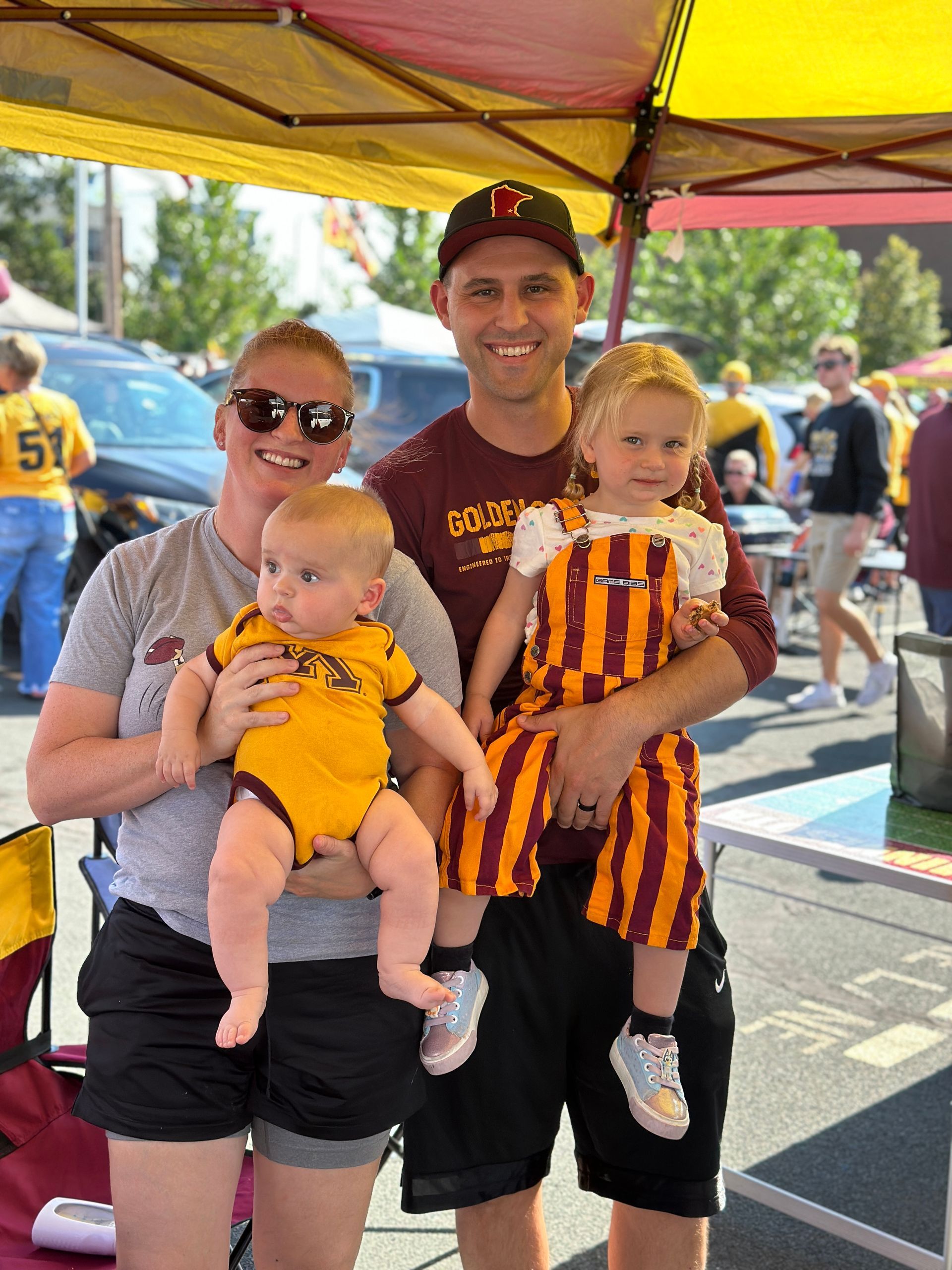 Family tailgating, wearing gold and maroon outfits, under a canopy.