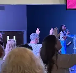 a group of people are standing in a room with their hands in the air .