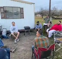 a group of men are sitting around a fire pit in front of a trailer .