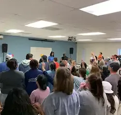 a large group of people are standing in a room with their hands in the air .