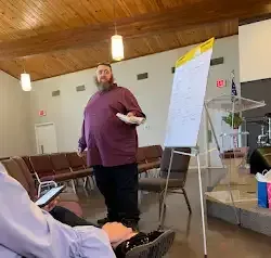 a man with a beard is standing in front of a whiteboard in a room .